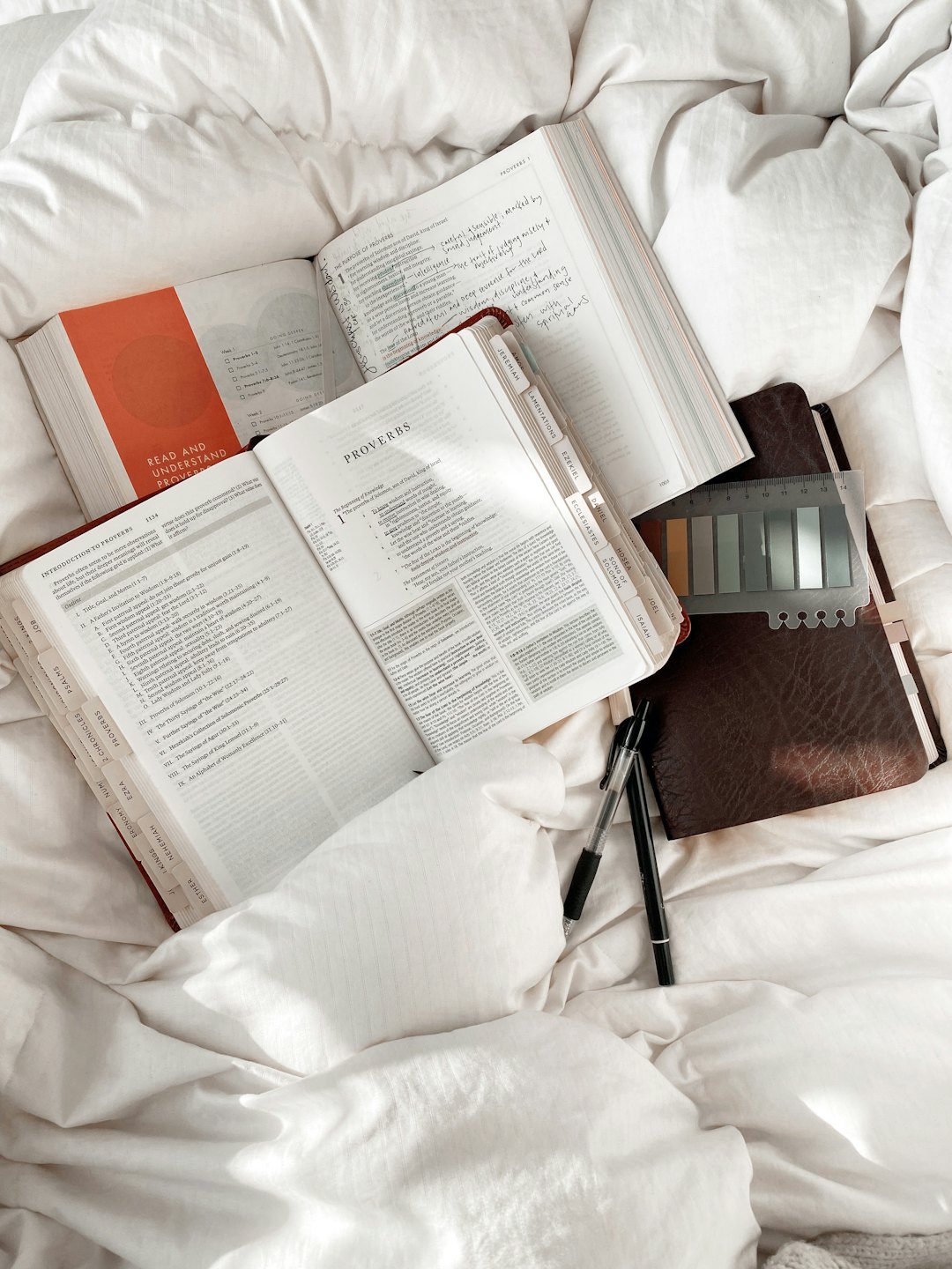 Open books and study supplies resting on white bed sheets.