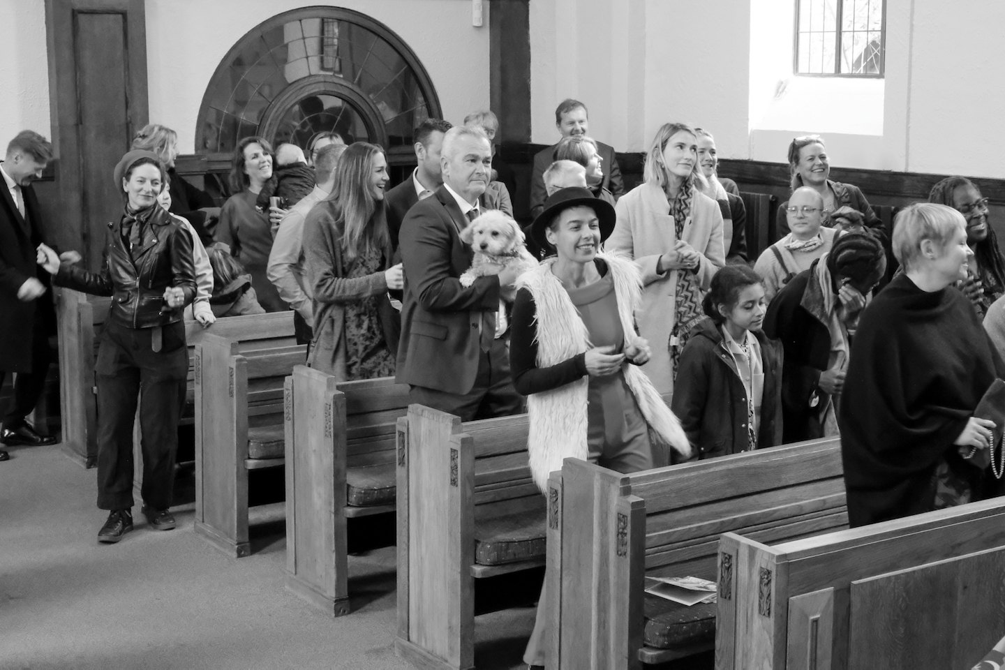 People mingling near wooden pews with a small dog.